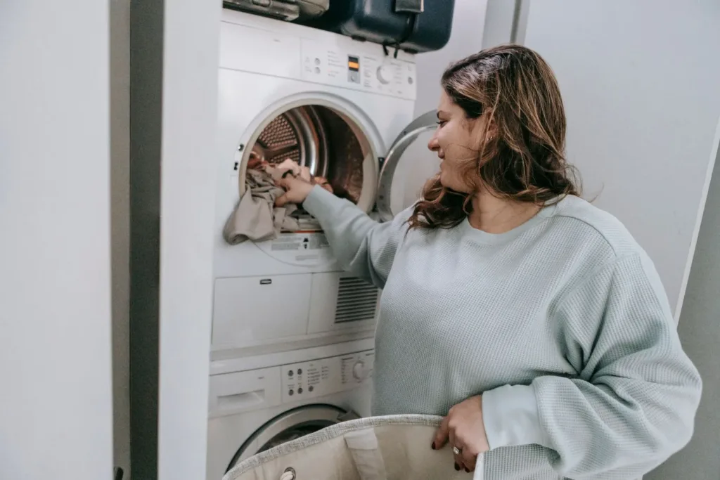 Mulher colocando roupas na máquina de lavar, representando o início rápido do processo de lavanderia.